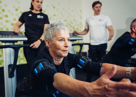 Frau trainiert mit EMS-Elektroden in der fitbox, Trainer im Hintergrund – Teaser zum EMS-Eignungstest